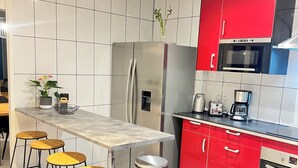 A modern kitchen with a central island, red cabinets, stainless steel appliances, and a tiled backsplash.
