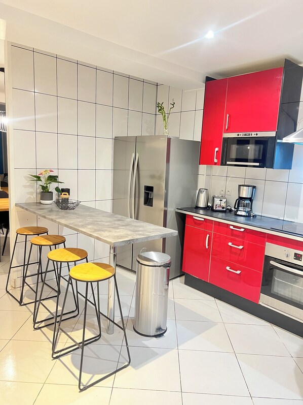 Une cuisine moderne dotée d’un îlot central, de meubles rouges, d’appareils électroménagers en acier inoxydable et d’un dosseret carrelé.