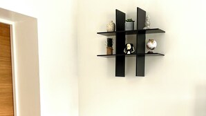 A corner of a room with a potted plant on a pedestal, a white door, and a black shelf with decorative items.