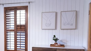 A room with wooden shutters, a white dresser with drawers, and two framed line drawings of hands on the wall. - Welcome to Rainbow at Folly House – Your Beachside Retreat Near Charleston! (Folly Beach)