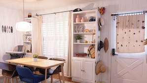 A cozy dining area with a wooden table and blue chairs, a white cabinet with decorative items, and a white door with a curtain. - Welcome to Rainbow at Folly House – Your Beachside Retreat Near Charleston! (Folly Beach)