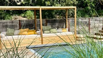 Une piscine avec une terrasse en bois et un espace détente agrémenté de coussins.