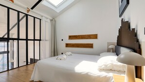 A modern hotel room with a large bed, a skylight, a wooden headboard, and a view of the city.