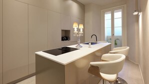 A modern kitchen with a central island, two white chairs, and a built-in coffee machine. - Luxurious 3 Bedroom Apartment near Pantheon (Roma)