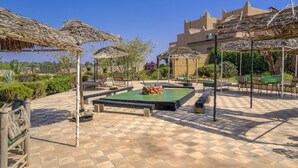 Un cortile con piscina, posti a sedere all'aperto e ombrelloni di paglia.