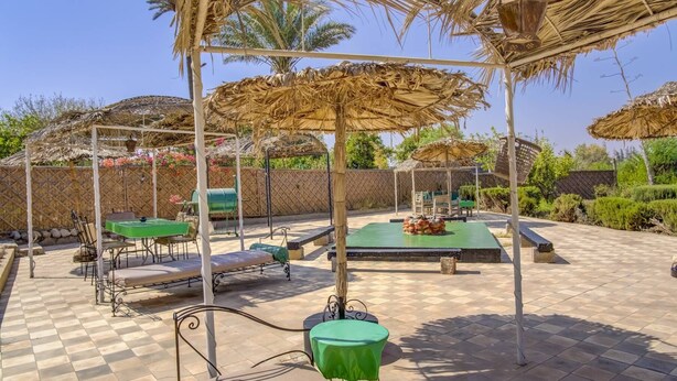 Una terrazza esterna con ombrelloni di paglia, tavoli e sedie in metallo.