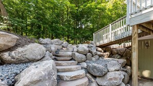 A stone staircase leading up to a wooden deck with a railing, surrounded by large rocks and greenery. - Maple Lake Hideaway! (Longville)
