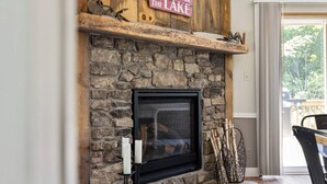 A stone fireplace with a sign above it, a window, and a view of trees outside. - Maple Lake Hideaway! (Longville)