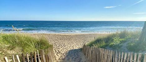 Walk along the beach pathway, bordered by a fence, to the ocean.