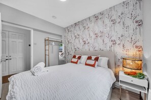 A bedroom with a bed, a nightstand, a lamp, and a floral wallpaper.