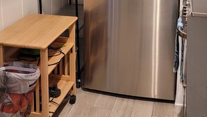 A compact kitchen with a stainless steel refrigerator, a wooden table, and a metal shelving unit.