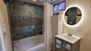 A bathroom with a bathtub, shower, vanity, and a round mirror.