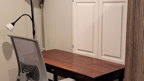 A room with a wooden table, a chair with wheels, a standing lamp, and a wardrobe.