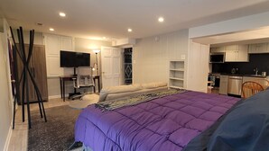 A hotel room with a large bed, a TV, a desk with a chair, a wardrobe, and a kitchenette.