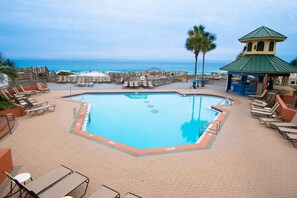 A pool area with lounge chairs, a small gazebo, and a view of the ocean.