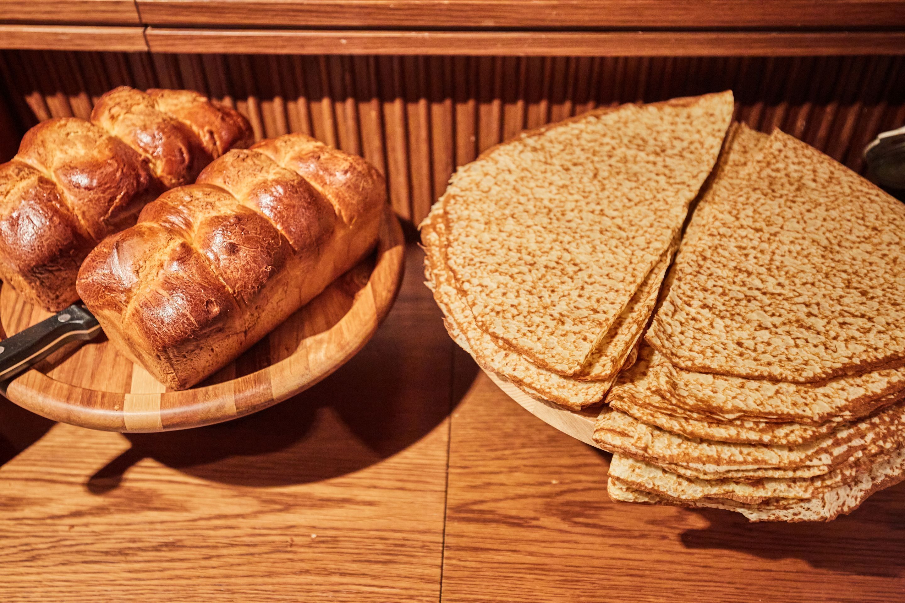 A wooden table with a loaf of bread and a stack of flatbreads.