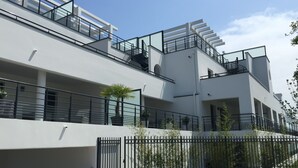 A modern multi-story building with balconies, a gated entrance, and a landscaped area with plants. - Villa Luxe 8p | Piscine & Plages à Pied (Anglet)