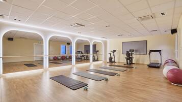 A spacious gym with wooden floors, exercise mats, and various fitness equipment.