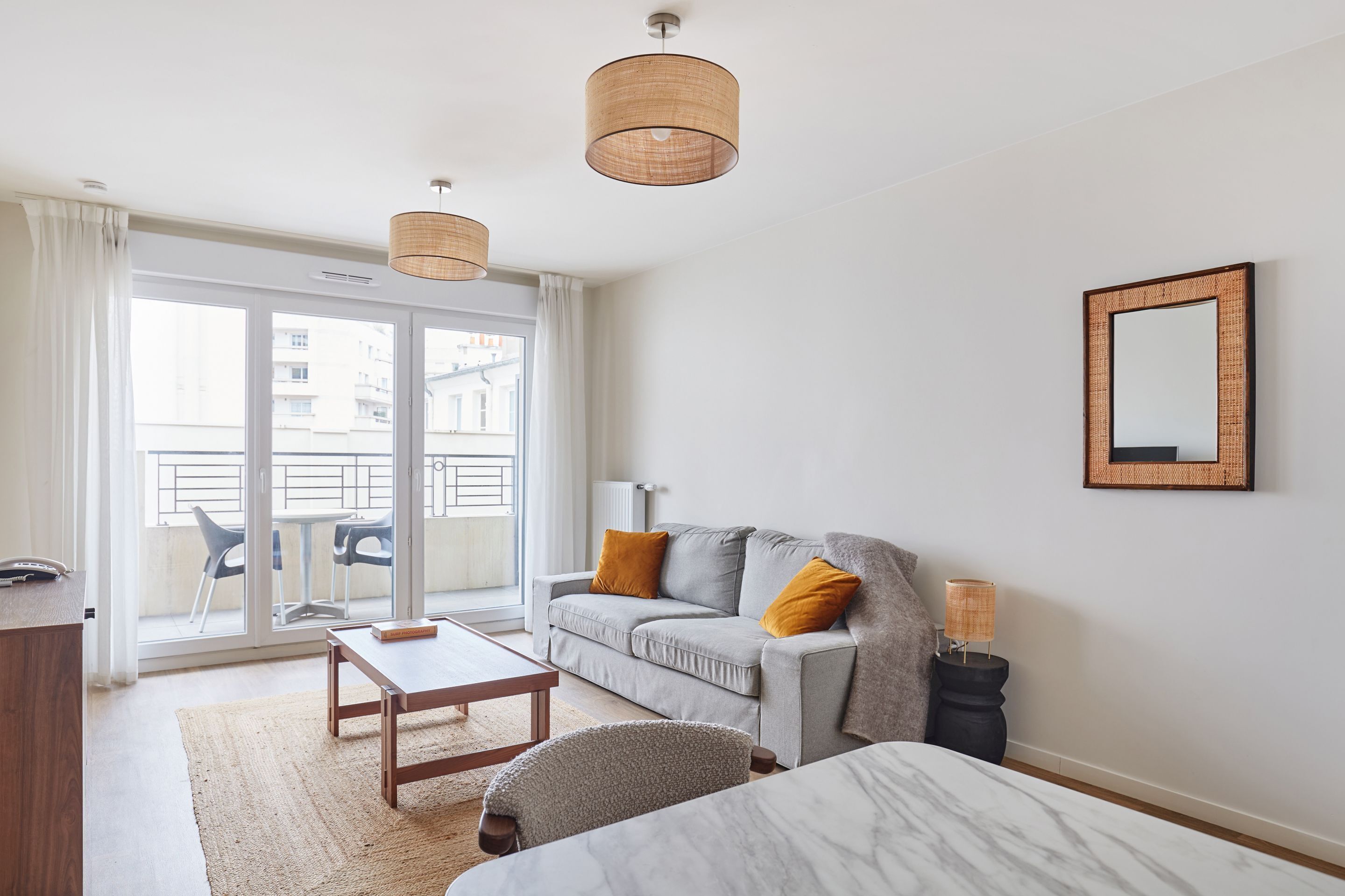 A modern living room with a grey sofa, wooden coffee table, and a large window with a view of buildings.