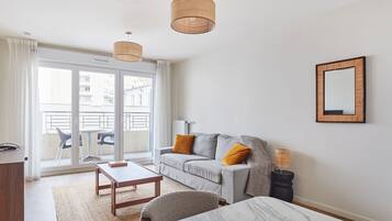 A modern living room with a grey sofa, wooden coffee table, and a large window with a view of buildings.