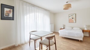 A modern bedroom with a bed, bedside tables, and a dining area with chairs. - Studio cosy à 5 min du train direct pour Paris (Levallois-Perret)