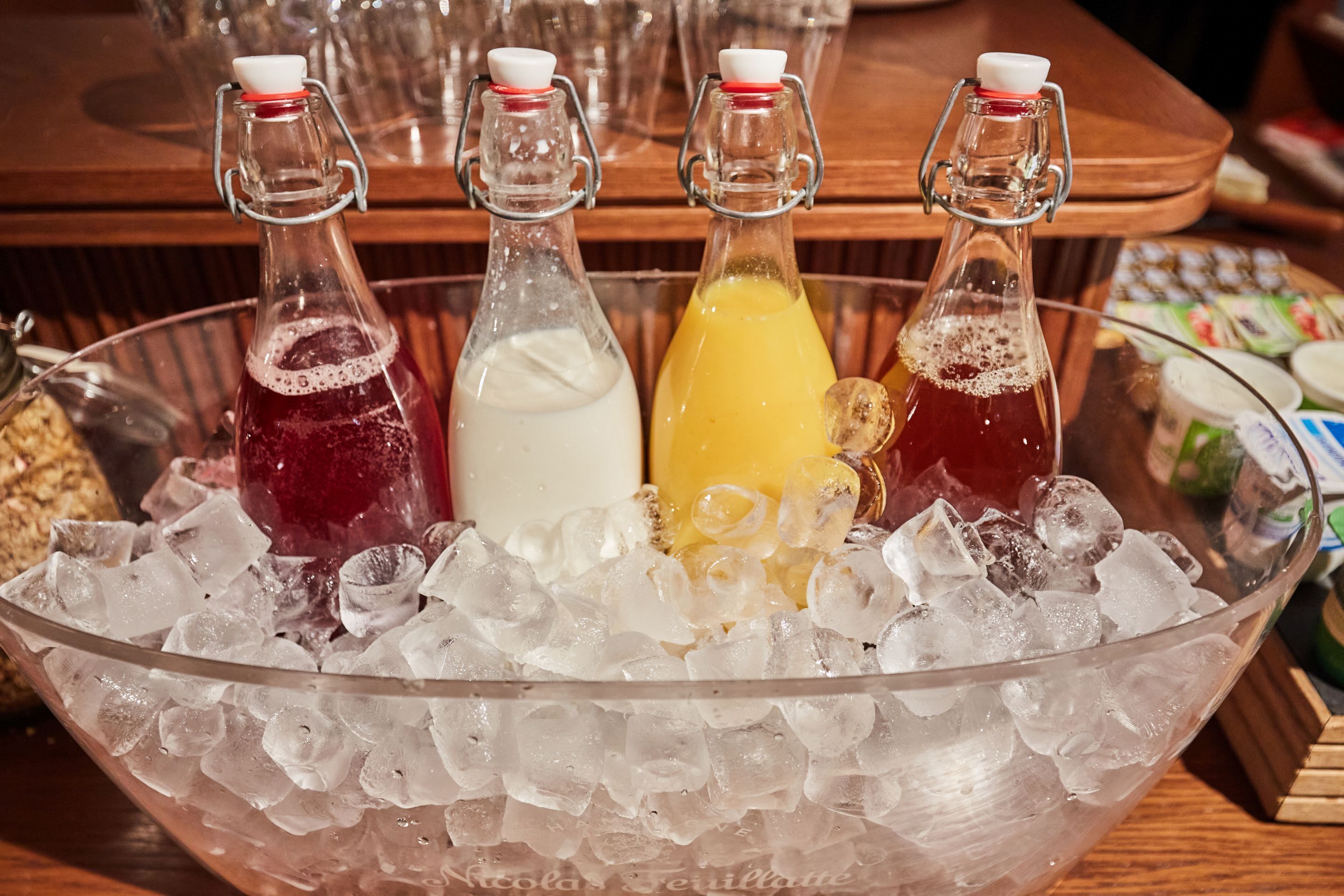 A large glass bowl filled with ice, containing four bottles of beverages.