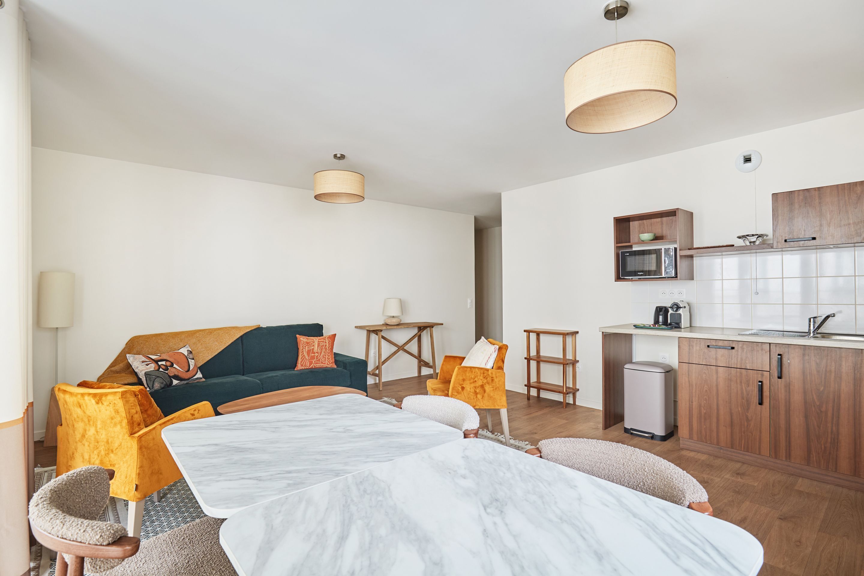 Een moderne woonkamer met een bank, stoelen, een eettafel en een keuken met kasten en apparatuur.
