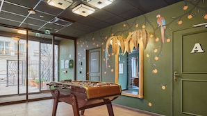 A room with a foosball table, a green door with the letter 'A', and a wall mural with a tree and fruit. - T3 familial 6 pers. | Train pour Paris à 5 min (Levallois-Perret)