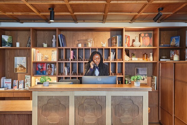 Un comptoir d’accueil avec un revêtement en bois, un ordinateur Dell et une variété de livres et d’objets décoratifs disposés sur des étagères.
