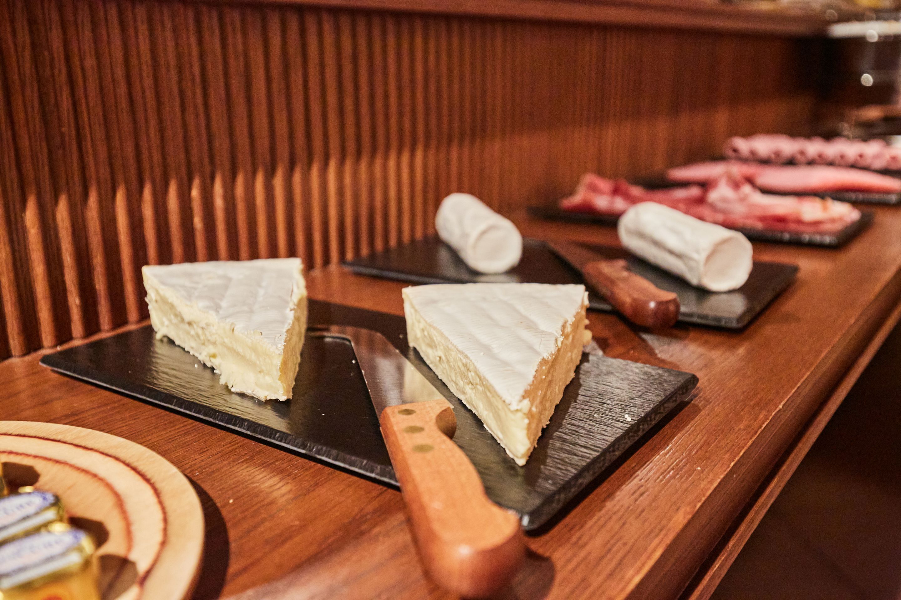 Un comptoir de bar en bois, avec un couteau et deux morceaux de gâteau blanc en forme de triangle, présentés sur des assiettes noires.