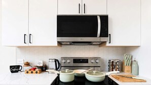 A modern kitchen with white cabinets, a microwave, a stove, and various cooking utensils.