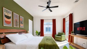 A hotel room with a bed, a TV, a ceiling fan, and artwork on the wall.