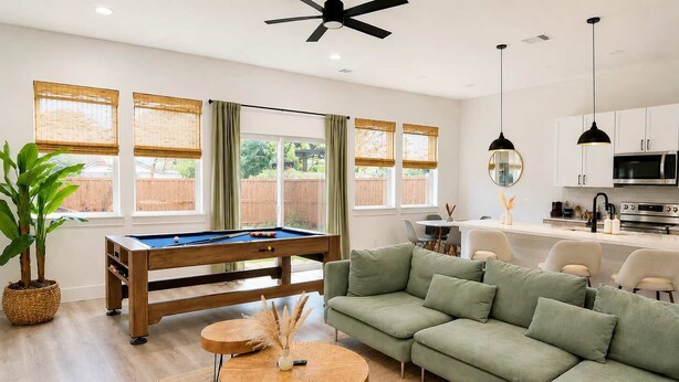 A modern living room with a pool table, green sofa, and a dining area with a white table and chairs.