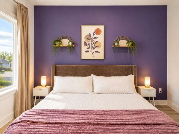 A bedroom with a large bed, two bedside lamps, a window with curtains, and wall-mounted sconces.