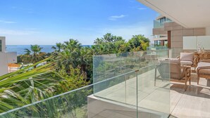 A modern balcony with a glass railing overlooking a lush garden and the sea. - Sapphire | Sea view - pool - terrace (Estepona)