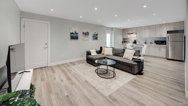 Un salon moderne avec un canapé gris, une table basse et un téléviseur. La pièce est dotée d’un plancher en bois et d’une porte blanche.
