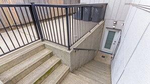 Un escalier en béton avec des rampes métalliques menant à une porte dotée d’un panneau en verre dépoli.