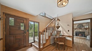 A wooden-floored interior with a staircase, a dining area, and a stone fireplace.