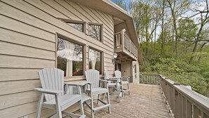 A wooden deck with Adirondack chairs and a railing overlooking a forested area.