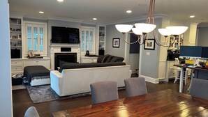 A modern living room with a fireplace, a sofa, a dining table, and a kitchen area with a TV and computer.