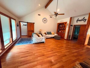 A spacious living room with wooden flooring, a ceiling fan, and a large window with blinds. - Private Pool Oasis, 4 Beds, Pet Friendly (Orange)