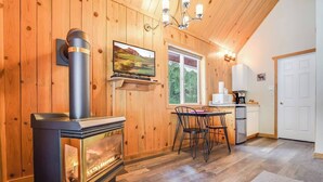 A cozy cabin interior with a wood stove, a dining area, a kitchen, and a large window. - Mount Adams Cozy Cabin Retreat (Trout Lake)
