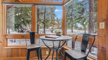 Una habitación acogedora con una mesa redonda y dos sillas, una ventana con vistas a un bosque nevado y paredes de madera.