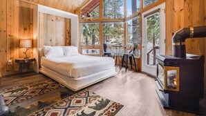 Una habitación de cabaña acogedora con cama, mesa, sillas, chimenea y ventanas amplias.