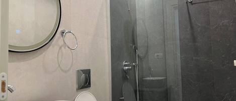 A modern bathroom with a large mirror, a freestanding toilet, a glass-enclosed shower, and a vessel sink.