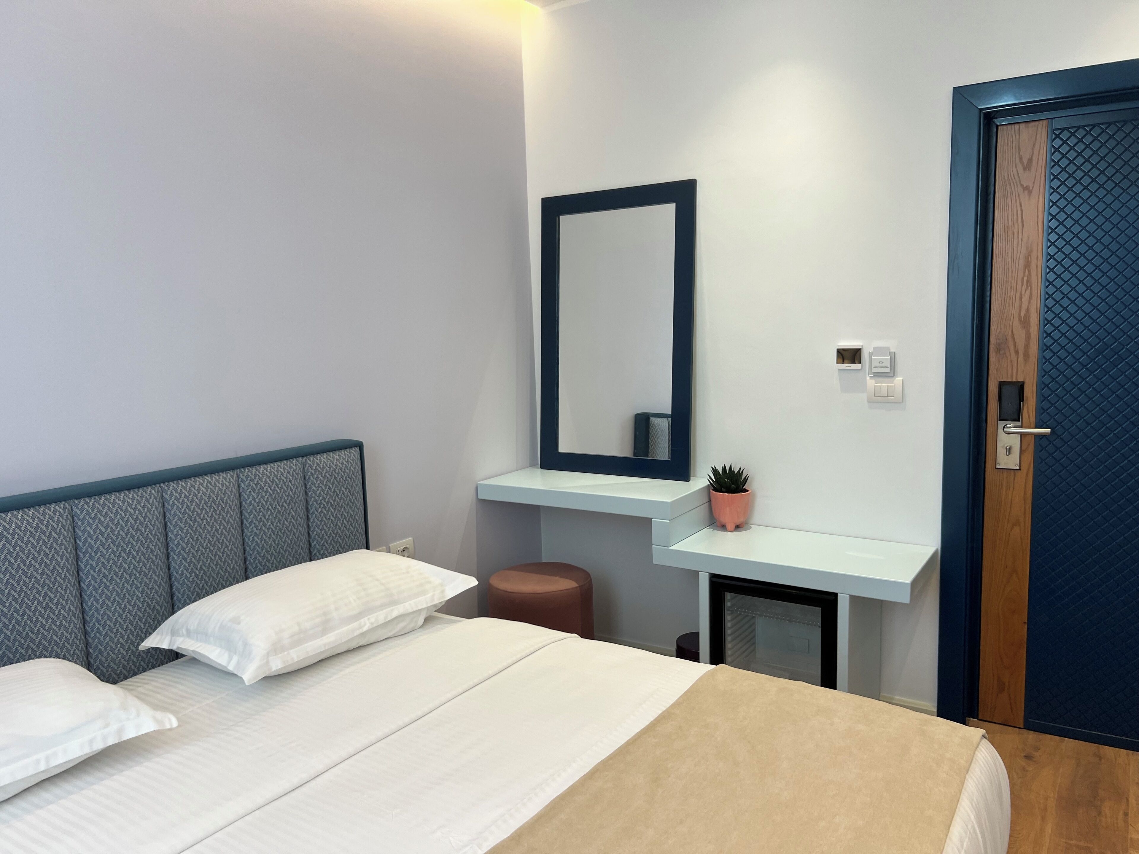 A modern hotel room with a bed, a nightstand, a mirror, and a door.