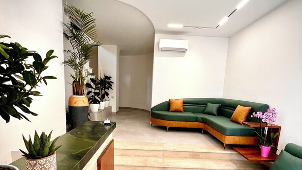 A modern living area with a green sectional sofa, a wooden reception desk, and potted plants. - The MONT BOUTIQUE HOTEL (Shkodër)