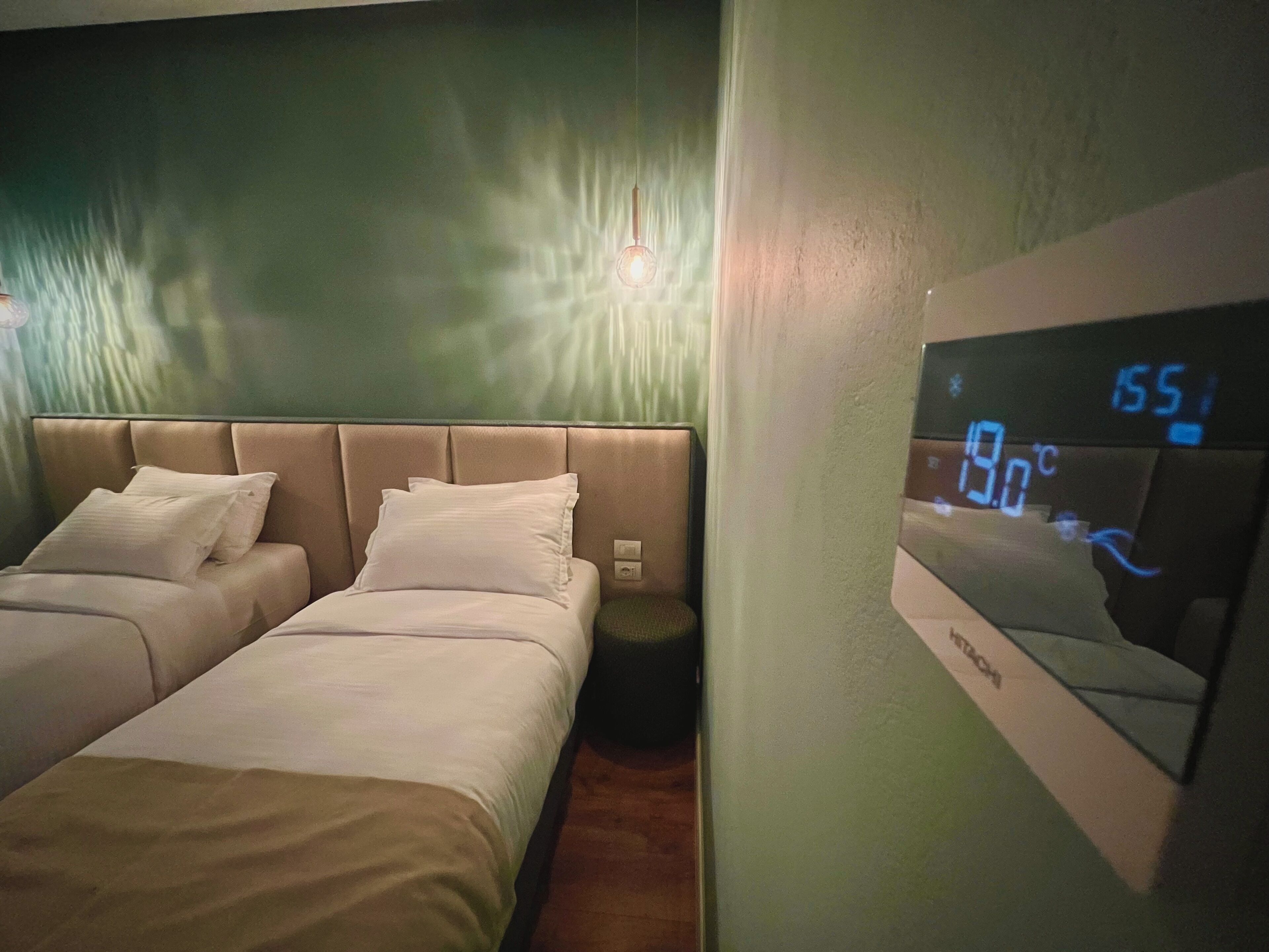 A hotel room with two beds, a digital thermostat, and a wall-mounted mirror.