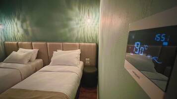 A hotel room with two beds, a digital thermostat, and a wall-mounted mirror.