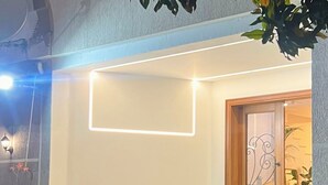 A modern entrance with a minimalist design, featuring a wooden door with decorative metalwork, a small outdoor seating area with a table and chairs, and a potted plant. - The MONT BOUTIQUE HOTEL (Shkodër)